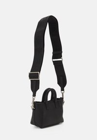 Mini borsa nera con un esterno in pelle liscia, doppi manici corti e una tracolla removibile con logo impresso e accessori in metallo.