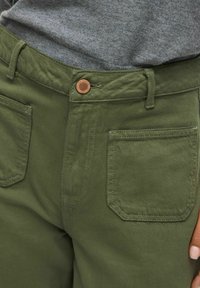 Pantaloni in cotone verde con chiusura a bottone, tasche laterali e una texture liscia. Dettagli di cucitura lungo le tasche e la vita.