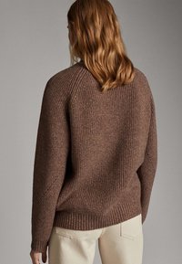 Maglione marrone a maglia con orlo a coste, caratterizzato da una vestibilità rilassata e dettagli in tessuto testurizzato, visto da dietro. Sono visibili pantaloni beige chiaro.