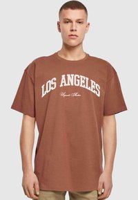 Brun oversized t-shirt med hvid "LOS ANGELES" tekst og mindre tekst nedenunder. Korte ærmer, rund halsudskæring og blød tekstur.