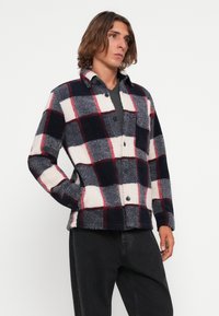 Karierte Fleece-Jacke in Marineblau, Weiß und Rot. Mit einer Knopfleiste, zwei Taschen und einer leicht strukturierten Oberfläche.