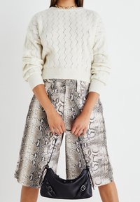 Maglione lavorato a maglia crema con motivo a zigzag e polsini a coste, abbinato a pantaloni corti con stampa animalier a serpente. Borsa nera con manici a spalla in mano.