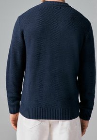 Granatowy sweter dzianinowy z textured wzorem, okrągłym dekoltem oraz ściągaczami przy mankietach i dolnej krawędzi. Tył swetra prezentuje się bezszwowo.