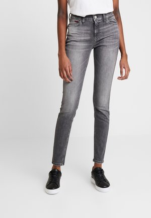 Jeans de talle alto, ajustados y de color gris con diseño desteñido, cinco bolsillos y cierre de botón. Combinados con zapatillas negras y una camisa blanca.