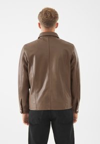 Bruine leren jas met een gestructureerde kraag, met een gladde textuur en nette naden, gecombineerd met zwarte broeken. Achteraanzicht weergegeven.