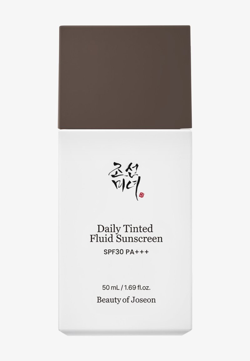 Bouteille rectangulaire blanche avec un bouchon marron. L'étiquette présente un texte noir et rouge : "Fluide teinté quotidien écran solaire SPF30 PA+++" avec le nom de la marque. 50 mL.