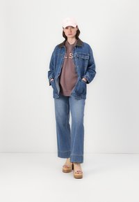 Jeans jakna s rjavim ovratnikom, siva majica s kapuco z napisom "Elias", široke modre kavbojke in bež platform sandali. Roza bejzbolska kapa.