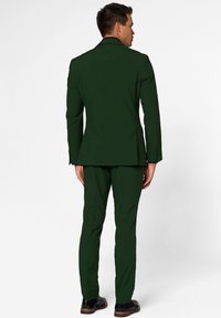 Completo verde scuro con giacca aderente e pantaloni slim, realizzato in tessuto liscio. Include cuciture sottili e scarpe eleganti nere.