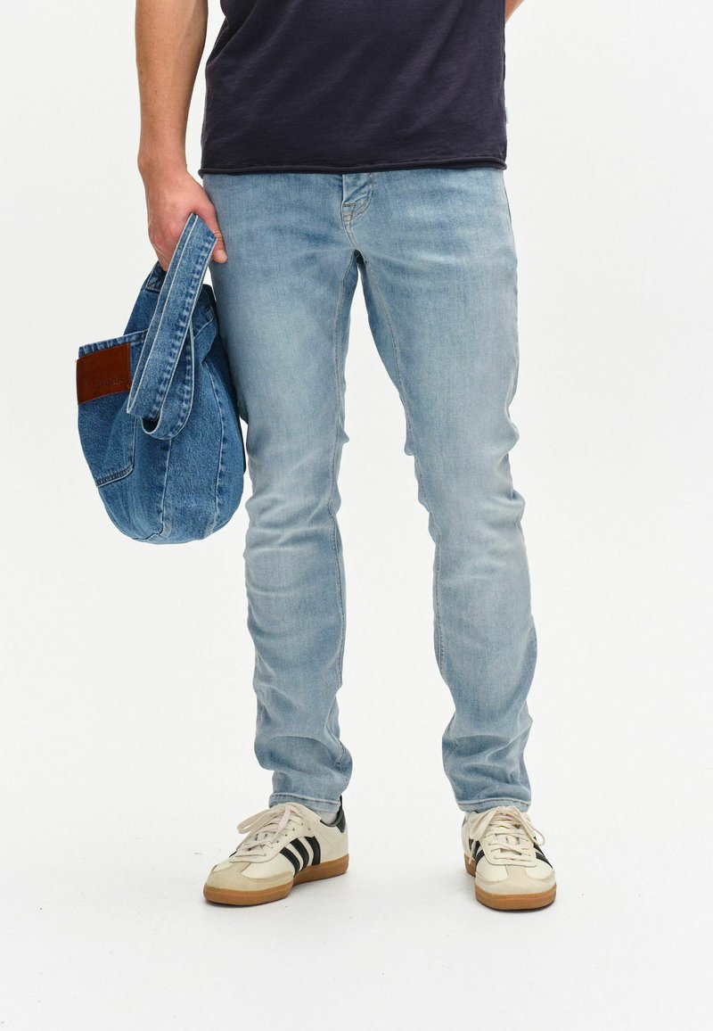 Svetlo modri traper hlače s ozkim krojem, v kombinaciji z belimi supergami z črnimi črtami, ki držijo modro traper torbo z rjavimi detajli.