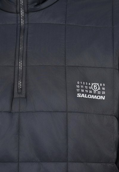 Černá prošívaná bunda s půlzipem a bílým logem Salomon a vytištěnými čísly na levé oblasti hrudi.