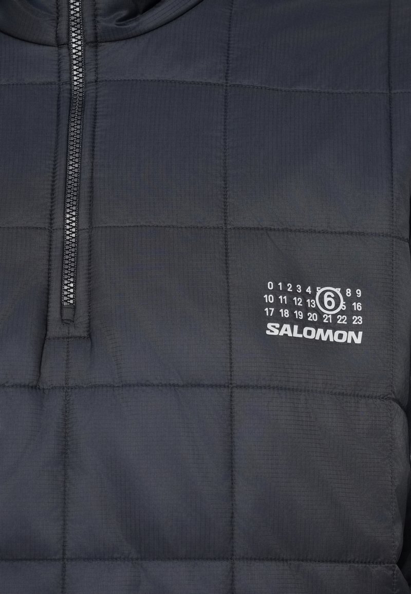 Schwarze gesteppte Jacke mit halbem Reißverschluss und weißem Salomon-Logo sowie Datumszahlen auf der linken Brustseite gedruckt.