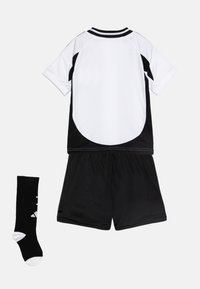 Equipo deportivo en blanco y negro que incluye una camiseta de manga corta con acentos negros, pantalones cortos negros y una calceta negra con detalles blancos.
