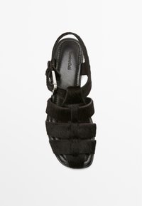 Sandal nera con cinturini, texture in pelliccia, cinturino alla caviglia regolabile e suola in pelle elegante. Presenta cinturini paralleli per un design moderno.