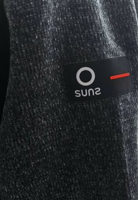 Tessuto grigio texturizzato con un'etichetta nera che mostra un cerchio bianco e una linea rossa, con la parola "suns."