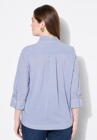 Blusa a strisce con collo alto, maniche a tre quarti e un fit rilassato. Strisce verticali blu e bianche, tessuto leggero.
