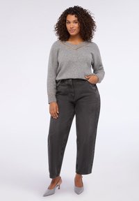 Suéter de punto gris con escote en V y detalle de cadena dorada, combinado con jeans de mezclilla negros de talle alto y zapatos de tacón gris.