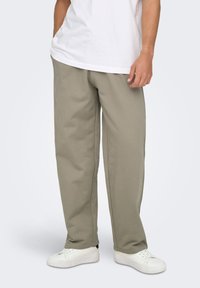 Pantalon large couleur kaki en mélange de coton doux, avec une coupe décontractée et des poches latérales, associé à des baskets blanches pour un contraste.