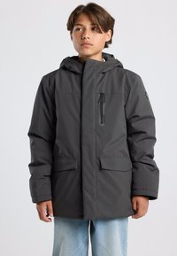 Harmaa, eristetty takki, jossa on huppu, etuvetoketju ja kaksi sivutaskua. Varustettu vetoketjullisella rintataskulla ja valmistettu sileästä materiaalista.