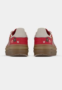 Červené tenisky s květinovou výšivkou, béžovými semišovými detaily a tlustou, texturovanou hnědou podrážkou. Mají bílé boční pruhy a polstrovaný límec.