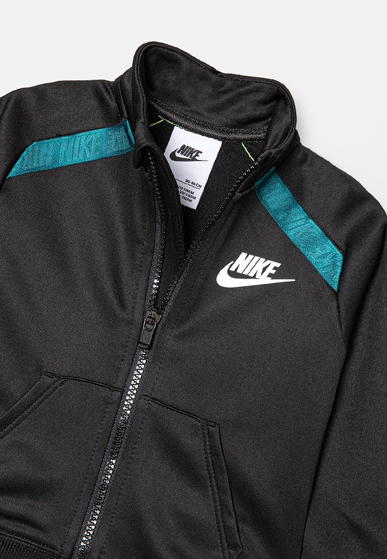 Schwarze Nike Zip-Jacke mit weißem Logo auf der Brust, türkisfarbenen Schulterstreifen und sichtbarem Größenetikett im Kragen.