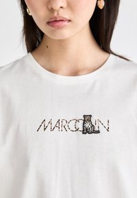 Bijela pamučna majica s crnom i smeškom leopardom izvezenim uz reč "MARCO" u stilu leopardove šare.