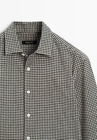 Camicia a quadri bianca e nera con bottoni frontali, colletto a punta, tessuto liscio e bottoni visibili lungo tutta la parte anteriore. Etichetta del marchio visibile.