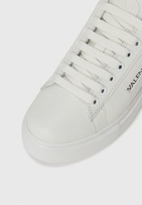 Hvite lær sneakers med rund tå, teksturert såle og flate hvite lisser. Har "VALENTINO" branding på siden.