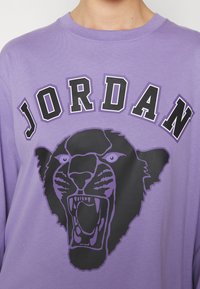 Långärmad lila t-shirt med en stor svart pantergrafik och texten "JORDAN" i fet stil ovanför. Mjuk bomullsmaterial.