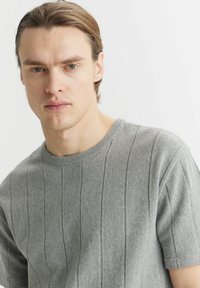 Szary sweter dzianinowy w paski z krótkimi rękawami, z okrągłym dekoltem i miękką fakturą. Pionowe linie dodają subtelnego detalu do projektu.