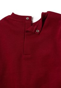 Top de punto rojo con un cuello acanalado, que presenta cierres de botones a presión en el cuello y una tela suave y texturizada.