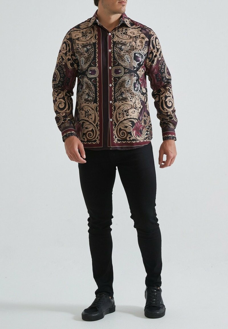 Chemise à boutons avec un motif paisley en noir, or et bordeaux. Manches longues, pantalon noir uni et chaussures noires complètent la tenue.