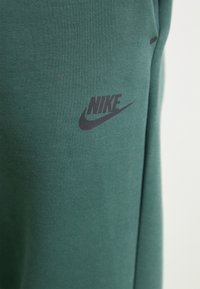 Zelená látka s černým logem Nike a žlutým taháním potisknutým na povrchu, zobrazující texturu a detaily materiálu.