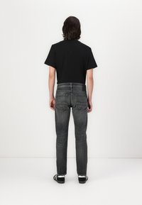 Zwart T-shirt met korte mouwen gecombineerd met donkergrijze slim-fit jeans. Opvallende stiksels op de achterzak en subtiele vervaging bij de knieën. Zwarte sneakers.
