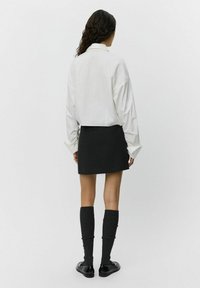 White oversized shirt with long sleeves, paired with a black mini skirt. Model wears knee-high grey socks and black loafers.