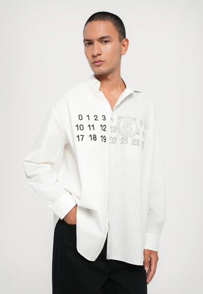 Weißes Hemd mit Knöpfen und halbgestreiftem Design, das auf einer Seite numerische Drucke und eine glatte Textur aufweist. Lange Ärmel und lockere Passform.