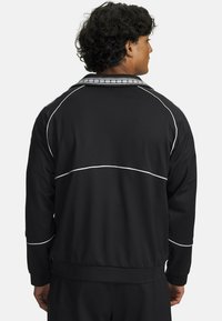 Black athletic jacket with white piping, featuring a ribbed collar and elastic cuffs. Smooth fabric with a slightly fitted design.
