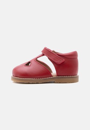 Scarpa da bambino in pelle rossa con cinturino a T e dettaglio traforato, suola beige e chiusura a strappo, mostrata di profilo su sfondo bianco.