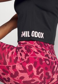 Zwarte atletische crop top met de tekst "SMIL ODOX", gecombineerd met hooggetailleerde legging met een roze luipaardprint en textuurdetails.