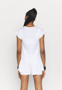 Top atlético blanco con mangas en forma de tapa, tejido texturizado y un ajuste relajado, combinado con pantalones cortos blancos que tienen un diseño en capas.