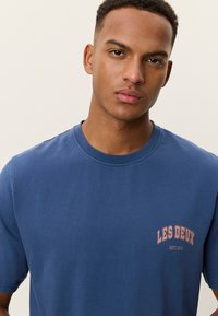 Μπλε ναυτικό βαμβακερό μπλουζάκι με κοντά μανίκια, με μικρό τυπωμένο λογότυπο σε ανοιχτό ροζ στην αριστερή πλευρά στο στήθος. Κλασικός στρογγυλός γιακαδισμός.