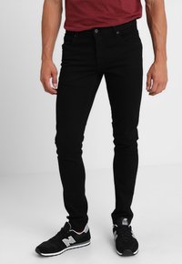 Jeans slim fit negros hechos de una mezcla de algodón, con cinco bolsillos y cierre de botón; combinados con zapatillas negras y una camisa burdeos.