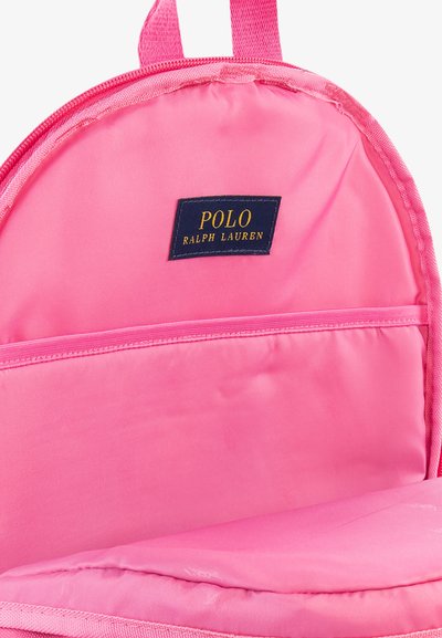 Ροζ σακίδιο με λείο νάιλον υλικό, διαθέτει ευρύχωρη εσωτερική τσέπη. Φέρει μια μπλε ετικέτα με την ένδειξη "POLO RALPH LAUREN" σε χρυσό κείμενο.