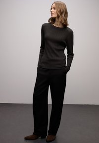 Maglione grigio scuro a coste con maniche lunghe, abbinato a pantaloni neri larghi e stivaletti in suede marrone. Design minimalista.