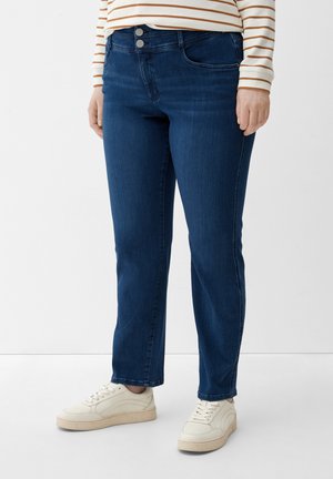 Jeans de mezclilla azul oscuro con corte ajustado, que cuentan con dos botones metálicos, bolsillos frontales y costuras sutiles. Combinados con zapatillas blancas.