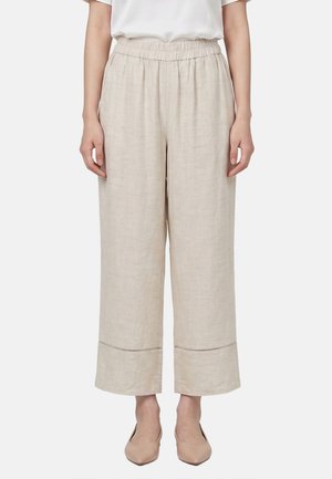Pantalon beige large et court avec taille élastique, porté avec des chaussures nude à bout pointu et un haut blanc.