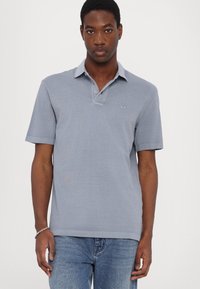 Light blue polo shirt with a collared neckline, short sleeves, and a small logo on the chest, made from a smooth fabric.