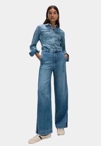 Camicia di denim e jeans a gamba larga di colore azzurro chiaro. Presenta una chiusura con bottoni, due tasche sul petto e una vita alta. Tessuto testurizzato, vestibilità rilassata.