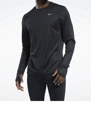 Mann trägt schwarzen langärmeligen Sportshirt mit Daumenlöchern und passende schwarze Hose, steht vor weißem Hintergrund.