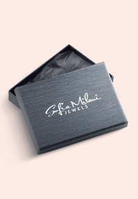 Grå rektangulär smyckesask med texturerad yta, med magnetstängning och vitt tryckt logo, delvis öppen, fodrad med svart silkespapper.