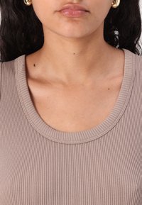 Ribbet, lysebrun tanktop med en bred u-formet hals. Stoffet er strukturert, mykt og tettsittende, noe som fremhever formen.